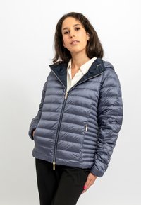 Giacca imbottita blu navy con chiusura con zip e tasche laterali. Dotata di cappuccio e polsini a coste. Texture liscia e lucida con cuciture orizzontali.