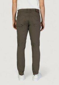 Pantaloni marroni slim-fit con tasche posteriori, dal look liscio e leggermente elasticizzati. Indossati con calzature bianche e una camicia bianca semplice.