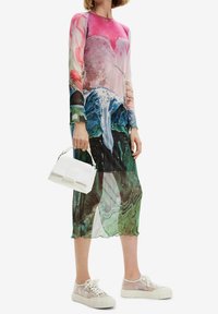 Robe à manches longues présentant un imprimé abstrait coloré en rose, bleu et vert, fabriquée en tissu transparent. Associée à un sac à main blanc et des baskets.