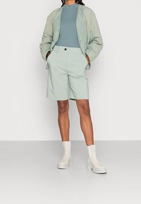 Hellgrüne gesteppte Jacke, tailliertes türkisfarbenes Oberteil und passende hellgrüne Shorts. Weiße Stiefeletten mit dicken Sohlen. Schlichtes, zeitgenössisches Design.