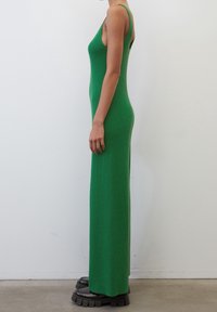 Abito a maglia verde con coste e silhouette aderente, caratterizzato da spalline sottili e design lungo, abbinato a calzature con suola spessa nere.