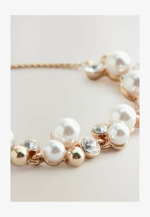 Perle- og krystalhalskæde, der har en kæde i gyldent tone, store hvide perler og små runde krystaller i et symmetrisk design.