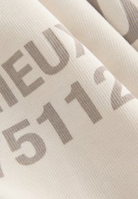 Cotton fabric in light cream, featuring large grey text with numbers and letters. Smooth texture, slightly stretched in folds.