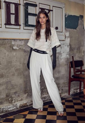 Pantaloni bianchi plissettati con una cintura con logo nero, abbinati a un top strutturato bianco sporco e lunghi guanti neri. Scarpe aperte scintillanti.