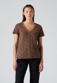 Brun v-hals t-skjorte med leopardmønster, med kort erm og en rød logo-patch på venstre bryst, laget av et mykt materiale.