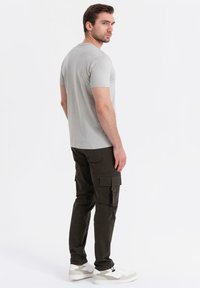 T-shirt grigio a maniche corte abbinato a pantaloni cargo verde scuro. Sneakers con accenti bianchi e beige. Design semplice e forma aderente.
