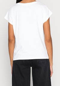 Camiseta blanca de manga corta con un ajuste relajado, cuello redondo y textura suave, combinada con pantalones negros de pierna ancha.