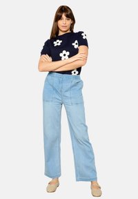 Suéter de manga corta azul marino con estampado floral blanco, combinado con pantalones de mezclilla de pierna ancha en azul claro. Textura suave y ajuste relajado.