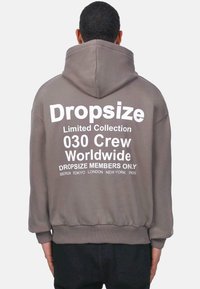 Grau Hoodie mit einem großen weißen Grafik auf dem Rücken. Der Text umfasst "Dropsize Limited Collection" und Städtenamen. Verfügt über eine Kapuze mit Kordelzug.