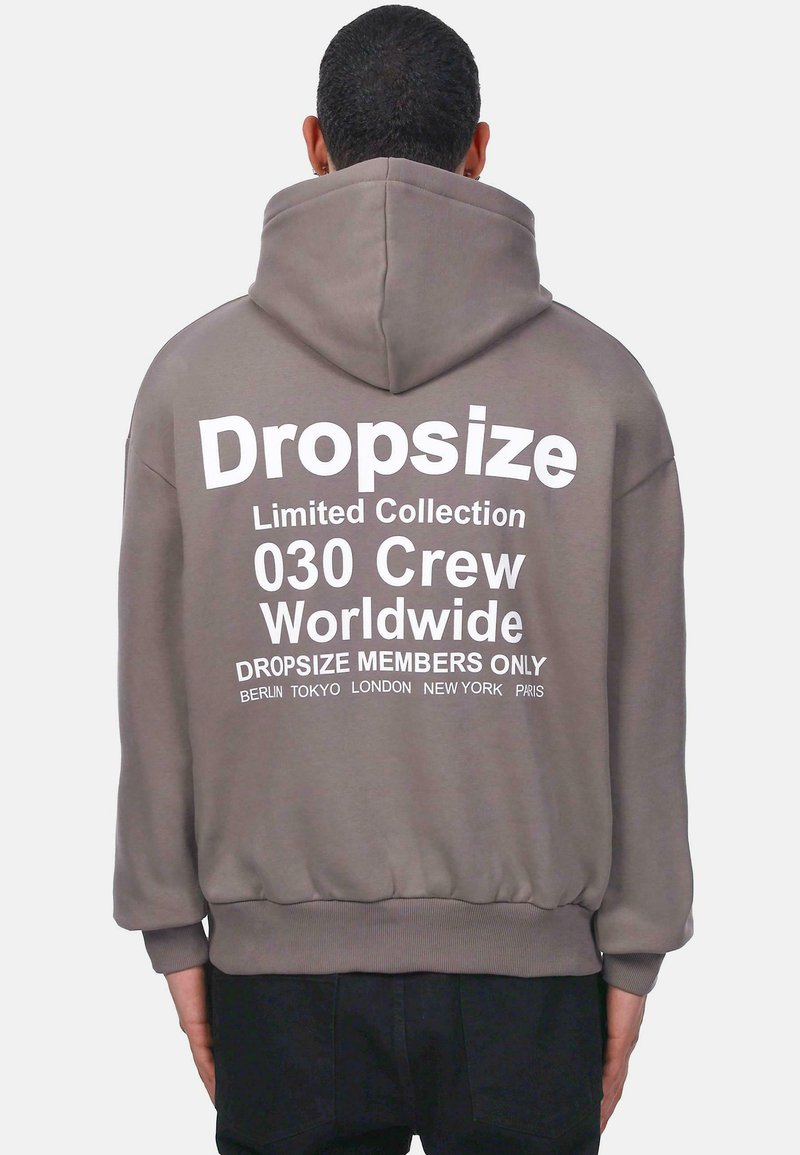 Pelēks krekls ar lielu balto grafiku aizmugurē. Uzraksti iekļauj "Dropsize Limited Collection" un pilsētu nosaukumus. Iezīmēts ar kapuci ar stingriem gredzeniem.