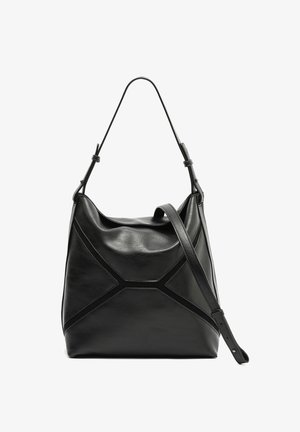 Črna usnjena torbica za ramo z enim zgornjim ročajem, geometrijskim vzorcem šivov in nastavljivim trakom za nošenje čez ramo na belem ozadju.