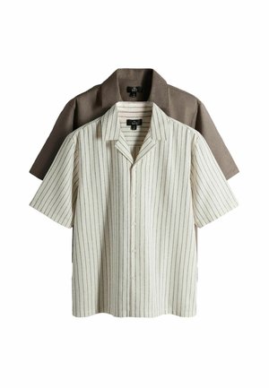 Két rövid ujjú, gombos ing, az egyik bézs vékony fekete függőleges csíkokkal, egy egyszínű barna ing fölött viselve, mindkettő gallérral és címkével.