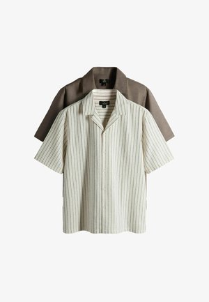 Zwei kurzärmelige Hemden zum Knöpfen, eines beige mit dünnen schwarzen vertikalen Streifen, darüber ein einfarbig braunes Hemd, beide mit Kragen und Etiketten.