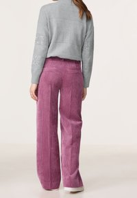 Ljusgrå, texturerad tröja med lång ärm och gnistrande detaljer, kombinerad med höga, vida, rosa kordbyxor.