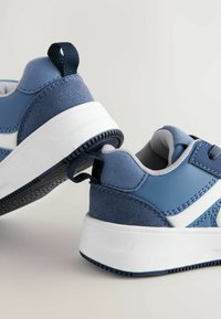 Niebieskie syntetyczne sneakersy z gładkim wykończeniem, siateczkową podszewką, białą podeszwą oraz teksturowanym piętą z uchwytem ułatwiającym zakładanie.