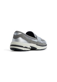 Zapatilla deportiva gris y plateada con parte superior de malla, cuello acolchado y correa de Velcro ajustable. Suela gruesa blanca y negra con textura.