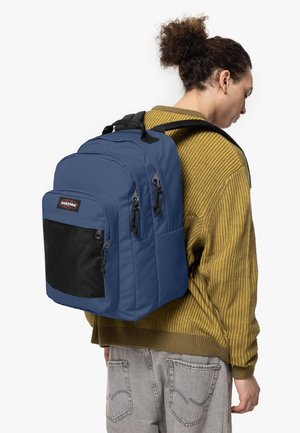 Mochila azul acolchada con bolsillo frontal de malla negra, doble cremallera y correas ajustables. Lleva sobre el hombro, hecha de tela duradera.