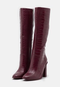 Bottes mi-mollet bordeaux avec texture crocodile, bout pointu et talon épais ; fermeture éclair latérale. Matériau synthétique lisse.