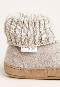 Gray felt slipper with a knitted beige cuff, featuring a label with "Gottstein." The sole is tan suede with visible stitching details.