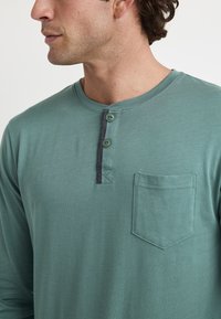 Langarm, groene henley shirt gemaakt van zacht materiaal, met twee knopen aan de voorkant, een grijze accenten op de placket en een borstzak.
