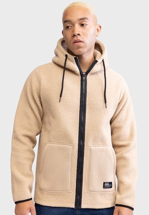 Felpa beige in pile con zip nera frontale, cappuccio con cordino e due grandi tasche frontali. Tessuto testurizzato con dettagli accentati in nero.