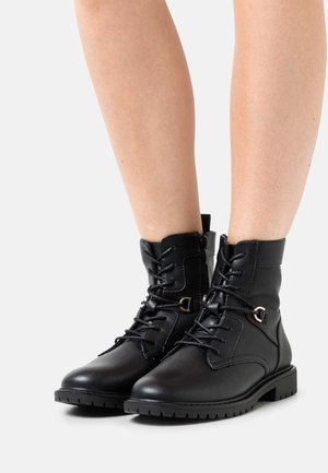 Bottines en cuir noir avec lacets et fermeture éclair sur le côté. Présentent une finition texturée, une semelle en caoutchouc et des accents en métal doré.