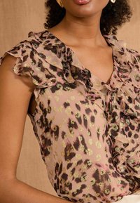 Sheer, pink blouse with black and gold leopard print, featuring ruffled edges and a v-neckline. Soft texture, fitted silhouette.