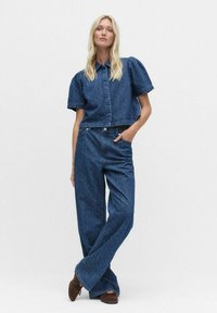 Jeansskjorta i denim med puffärmar och knappstängning, tillsammans med vida jeans med ett subtilt mönster, båda i mörkblått.