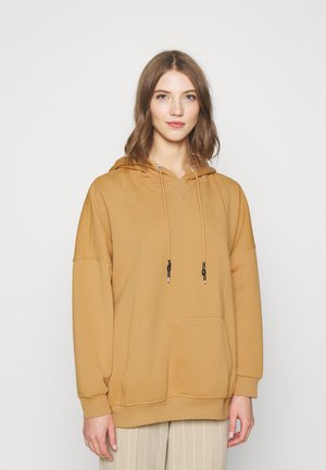 Hoodie boje senfa s V-izrezom, vezicama i prednjim džepom. Mekani, pamučno-sintetički materijal i oversized kroj s dugim rukavima.