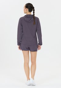 Lättviktsjacka med huva och shorts i en dämpad lila färg. Slät textur med sportig passform. Bärs med vita träningsskor.
