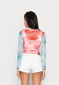 Camisola crop de manga longa com padrão floral em rosa e azul, com mangas transparentes e bainha em forma de onda; combinada com calções brancos desfiados.