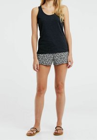Svart linne med rundad halsringning, matchat med svarta shorts med blommönster. Platta sandaler med tunna remmar fulländar outfiten.