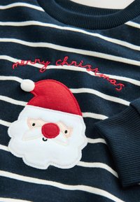 Granatowy sweter w paski z czerwoną i białą aplikacją Świętego Mikołaja. Zawiera wyszywankę "wesołych świąt" w kolorze czerwonym. Miękki, przytulny materiał z ściągaczami przy rękawach.