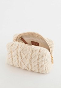 Kremowa dziergana sakiewka z wzorem warkocza, złotym zamkiem błyskawicznym i skórzanym akcentem. Wnętrze wyłożone beżową tkaniną, wyposażone w małą kieszonkę na zamek.