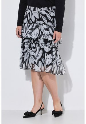 Donna che indossa una gonna a balze floreale bianca e nera con strati trasparenti e décolleté nere slingback con grandi fiocchi.