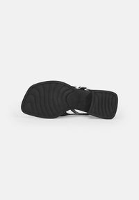 Black sandal with a smooth rubber sole; features a textured pattern, wide strap design, and an adjustable ankle buckle for secure fit.