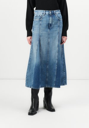 Denim maxi-skjørt med en lys til mørk blå gradient, A-linjeform, sydde paneler og sideslits. Kombinert med svarte ankelstøvler.