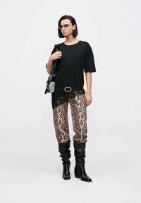 Černé tričko s krajkovým lemem, kalhoty s leopardím potiskem a černé kozačky po kolena. Doplňky zahrnují černý pásek a kabelku přes rameno.