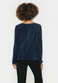 Námornícky plisovaný blúzka s dlhými rukávmi, zaobleným výstrihom a jemnou textúrou. Voľný strih s naťahovacími manžetami, ktorý sa končí pri bokoch.