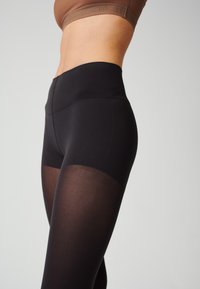 Leggings noirs taille haute en tissu lisse et extensible avec un panneau transparent au bas de la jambe, dotés d'une ceinture solide.
