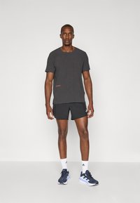 Mørkegrå kortermet treningsskjorte med rund hals og et subtilt teksturmønster, kombinert med svarte shorts og marineblå løpesko.