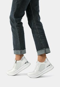 Sneakers bianchi con accenti metallici, chiusura a zip e pannelli laterali testurizzati. Abbinati a jeans scuri arrotolati per un look casual.