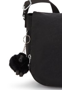 Schwarze Stofftasche mit Klappe, ausgestattet mit einem Metallreißverschluss und einem flauschigen schwarzen Gorilla-Schlüsselanhänger, der an einer silbernen Kette befestigt ist.