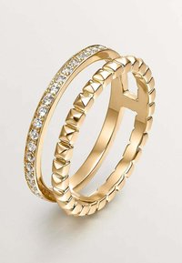 Anillos de oro, uno con una fila de piedras preciosas claras y otro con un diseño texturizado y acanalado. Ambos anillos tienen un acabado pulido.