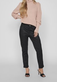 Pantalones casuales negros con textura suave y bolsillos frontales, combinados con un cuello de tortuga de punto rosa claro con mangas abullonadas.