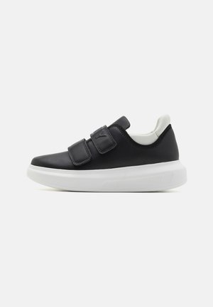 Black sneaker with a smooth leather upper, two adjustable Velcro straps, white sole, rounded toe, and subtle branding on the heel.