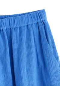 Blå strukturerade tygbyxor med elastisk midja och fickor, med en krinklad design för en avslappnad look.