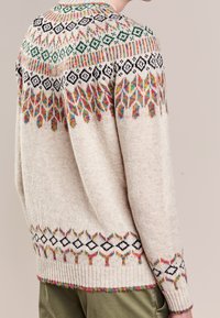 Pletený svetr béžové barvy s vícebarevnými geometrickými vzory na ramenou a ve spodním lemu. Obsahuje ribbované manžety a vysoký límec.
