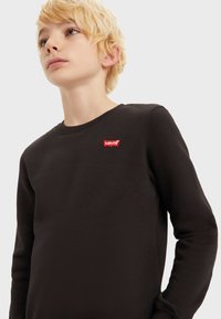 Sudadera negra de algodón suave, con cuello redondo y puños acanalados. Etiqueta del logo rojo de Levi's en la parte superior izquierda del pecho.