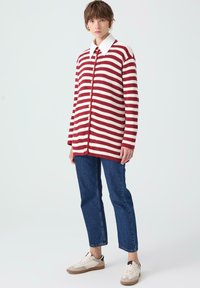 Raudonai ir balvai dryžuotas megztinis su mygtukais, oversized modelis, klasikinis baltas krutinės apykaklė, derinamas su mėlynais džinsais ir sportinėmis bateliais.